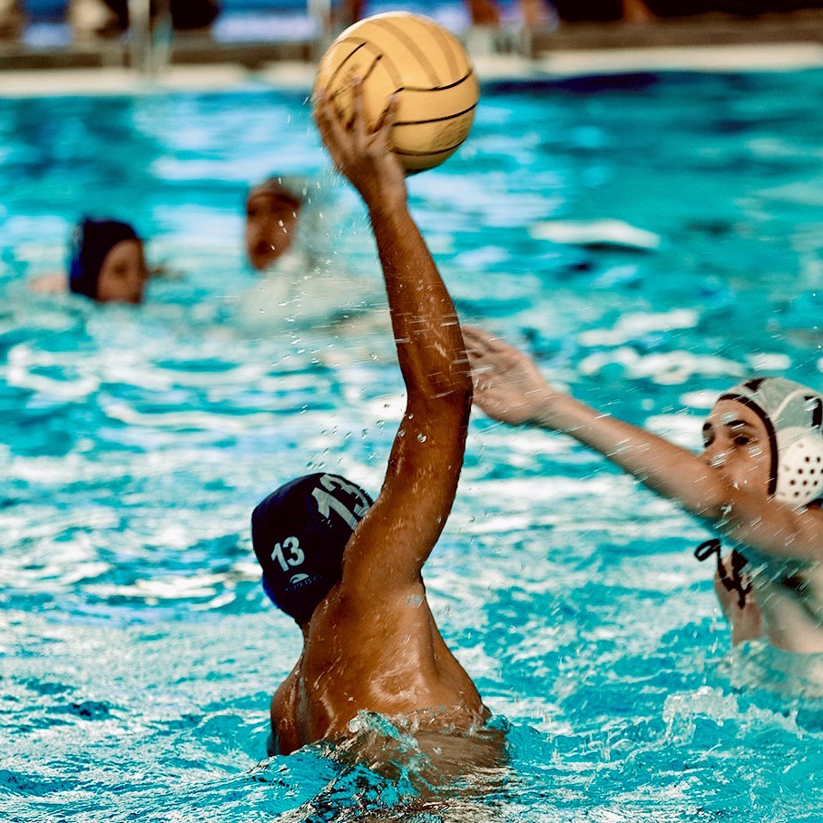Advait Johari playing water polo and reaching to pass the ball.